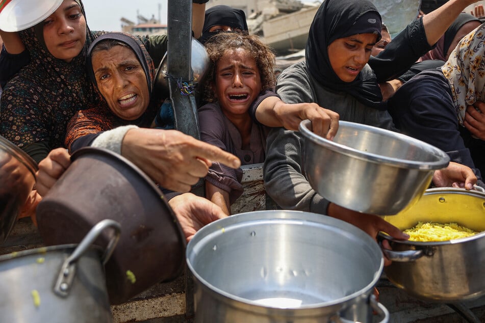A Palestinian girl cries as she tries to receive cooked meals along with others from a food distribution center in Gaza City on August 13, 2025.