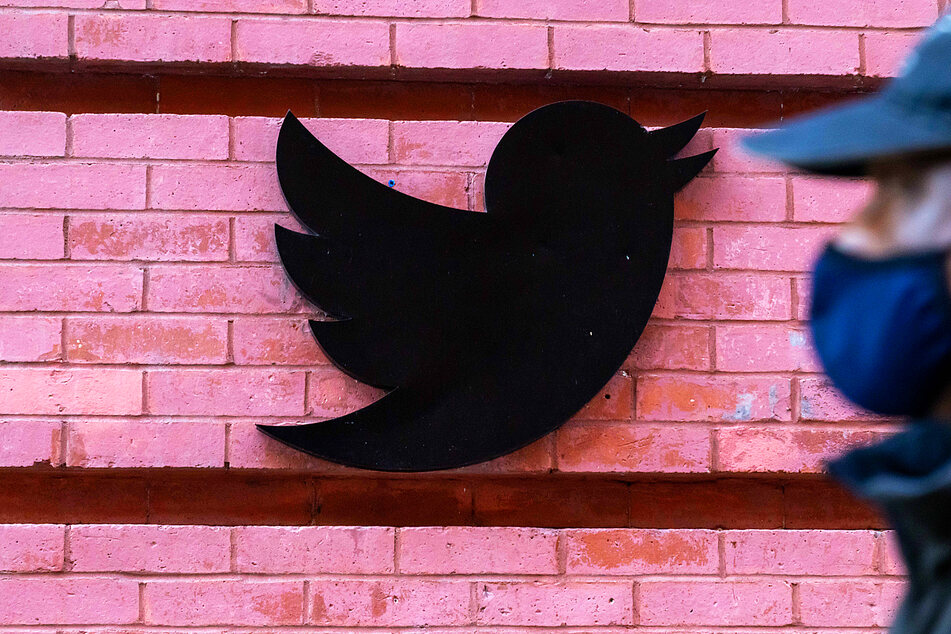 A man wearing a face mask walks past a Twitter logo outside New York City headquarters.