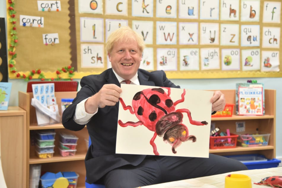 Boris Johnson hält bei einem Besuch der Discovery School in der Grafschaft Kent ein selbstgemaltes Bild mit einem Marienkäfer hoch.