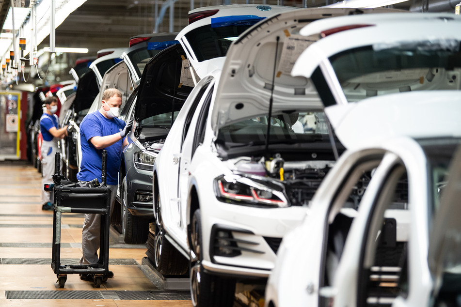 Ein Mitarbeiter setzt mit einem Mund- und Nasenschutz in der Produktion neben einem Auto.