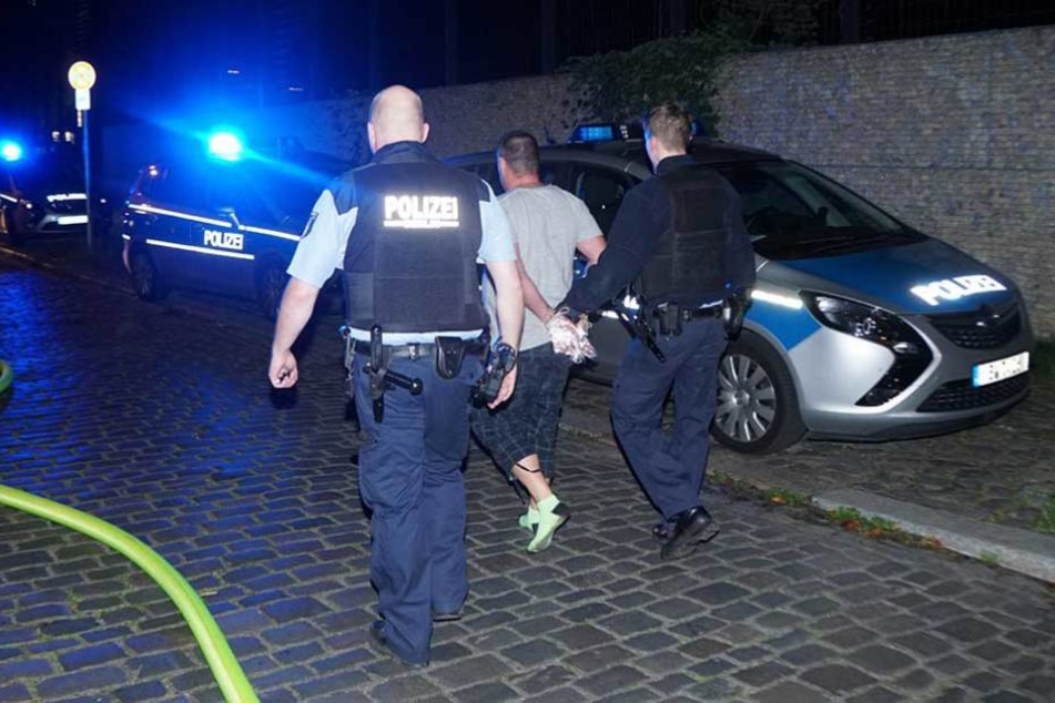 Polizisten führen den Verhafteten ab und bringen ihn zum Auto.