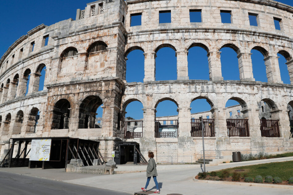 Eine arbeitslose Fremdenführerin geht am römischen Amphitheater vorbei, das normalerweise von Touristen überfüllt wäre.