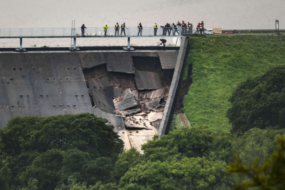 Menschen bilden über dem beschädigter Teil eines Staudamms am Toddbrook Reservoir eine Menschenkette um Sandsäcke auszulegen.