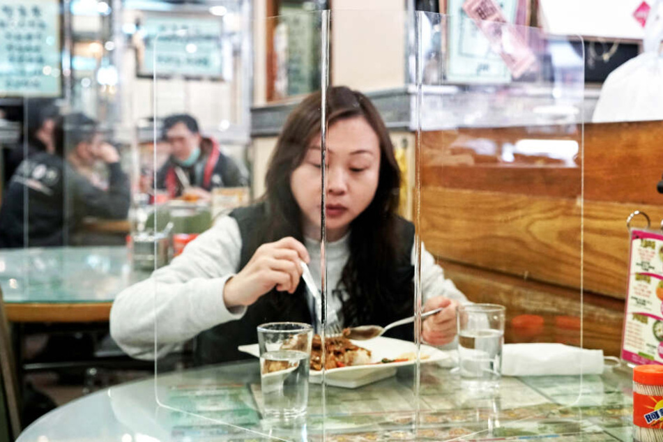 Eine Kundin sitzt hinter einer Plexiglaswand beim Mittagessen.