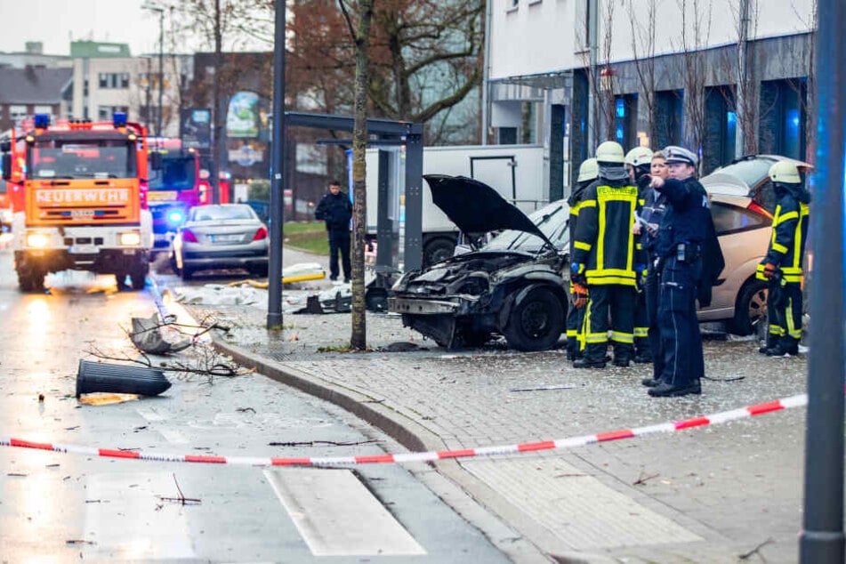 Polizisten und Feuerwehrleute stehenden neben dem beschädigten Auto an einer Bushaltestelle.
