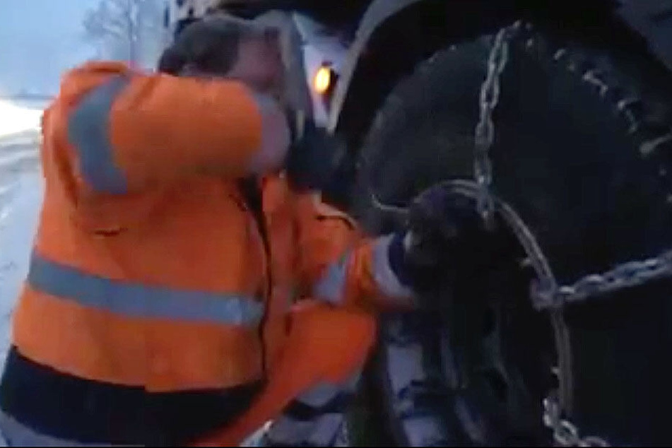 Der Lkw-Fahrer zieht Schneeketten auf.