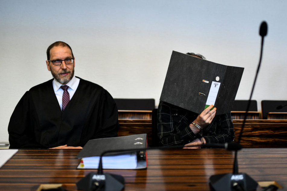 Der wegen Kindesmissbrauchs angeklagte Jürgen W. aus der Schweiz sitzt mit einem Ordner vor dem Gesicht in einem Saal des Landgerichts neben seinem Anwalt Robert Phleps. Heute wird der Hauptbeschuldigte als Zeuge befragt. (Archivbild)