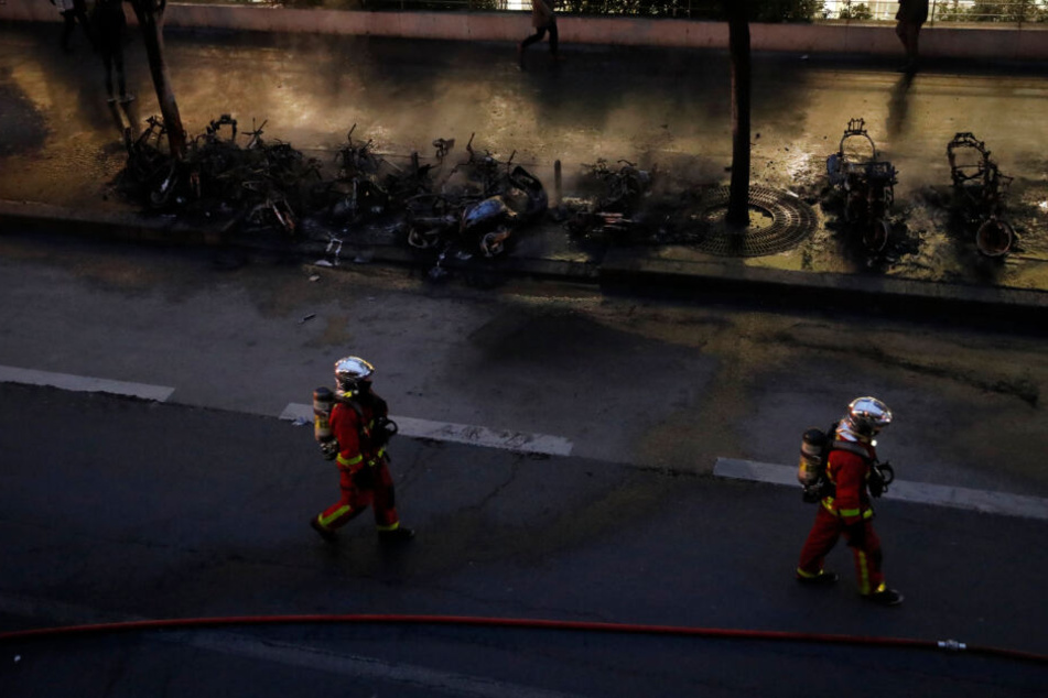 Einsatzkräfte der Feuerwehr gehen an verbrannten Motorrädern vorbei.