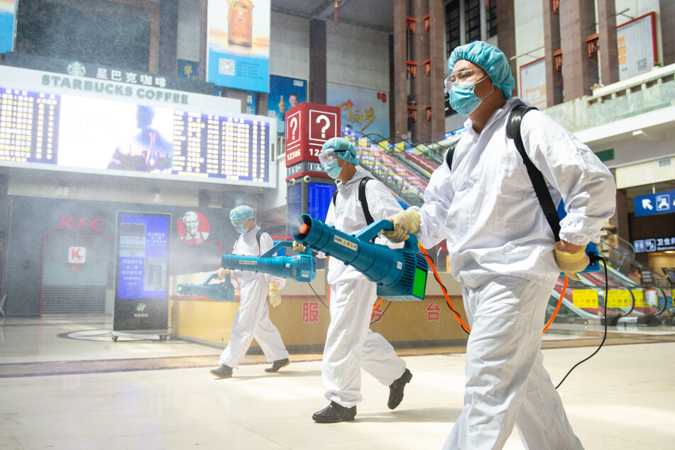 China, Peking: Arbeiter in Schutzkleidung desinfizieren einen Bahnhof.