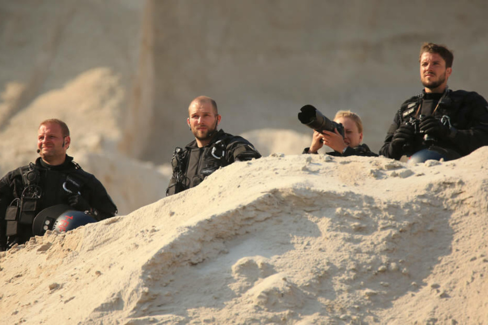 Polizisten stehen in der Braunkohlengrube Garzweiler hinter einem Hügel, eine Polizistin hält eine Fotokamera.