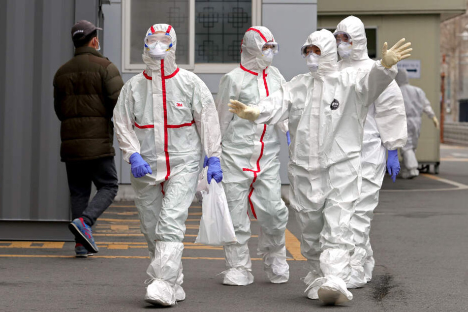 Medizinische Mitarbeiter in Schutzkleidung gehen über eine Straße, um zur Arbeit in ein Krankenhaus in Daegu (Südkorea) zu gelangen.