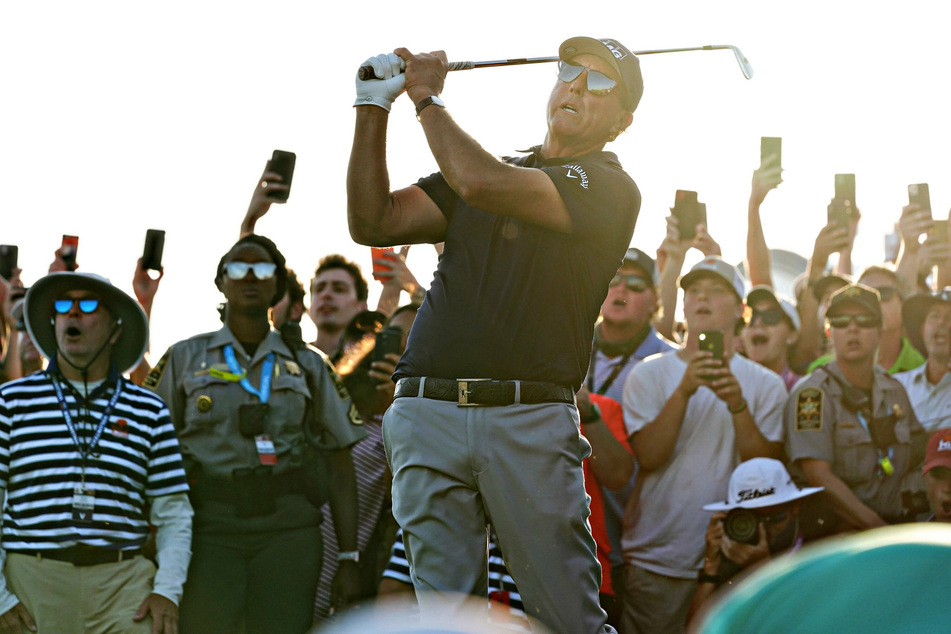 Phil Mickelson takes a shot down the 18th fairway surrounded by a crowd of cheering fans.