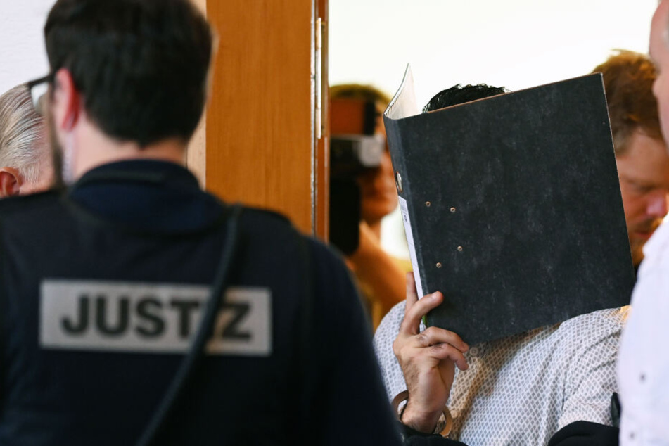 Einer von elf Angeklagten wird vor dem Prozessbeginn von einem Justizbeamten in einen Gerichtssaal im Landgericht gebracht. (Archivbild)