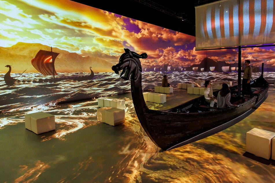 Das Herzstück der Ausstellung ist die immersive Show. Mitten im Raum erhebt sich ein rekonstruiertes Langschiff, das den Gästen als Sitzplatz dient und durch immersive Visuals, Licht- und Soundeffekte auch selbst Teil der Inszenierung wird.