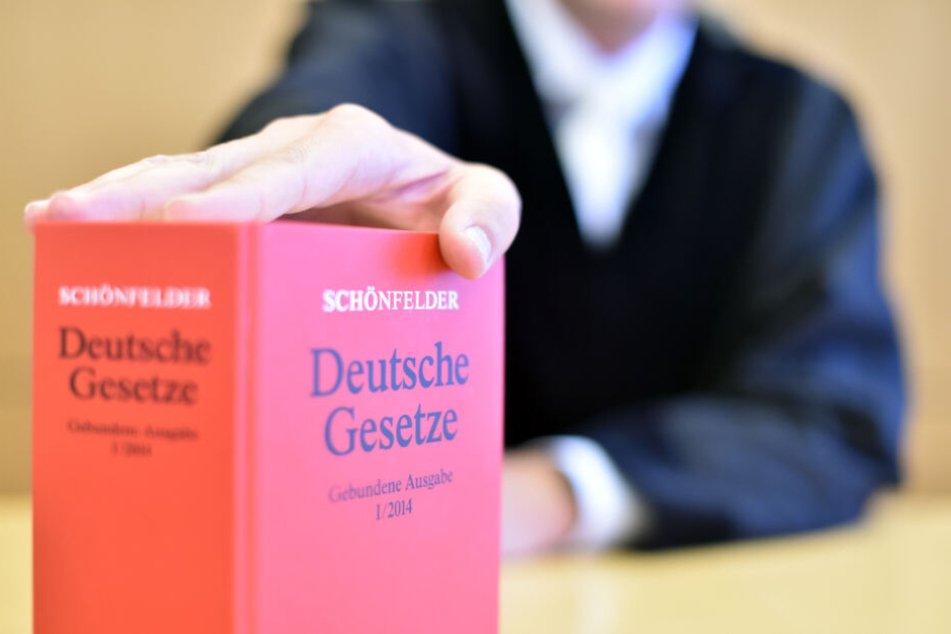 Ein Richter sitzt beim Oberlandesgericht auf der Richterbank und hält ein Buch mit den Deutschen Gesetzen.
