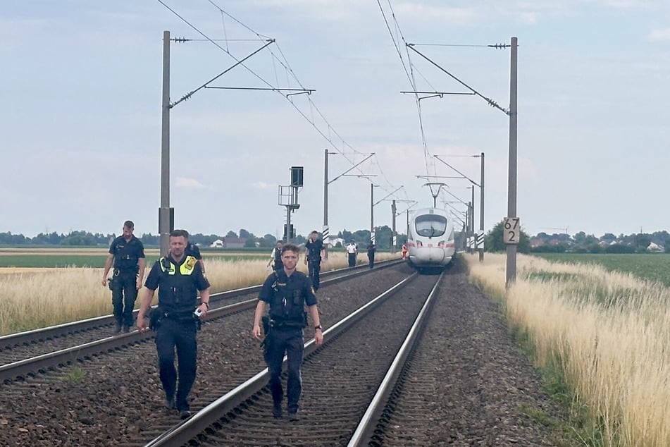 Polizisten gehen am Gleisbett vor dem Zug bei Straßkirchen entlang.