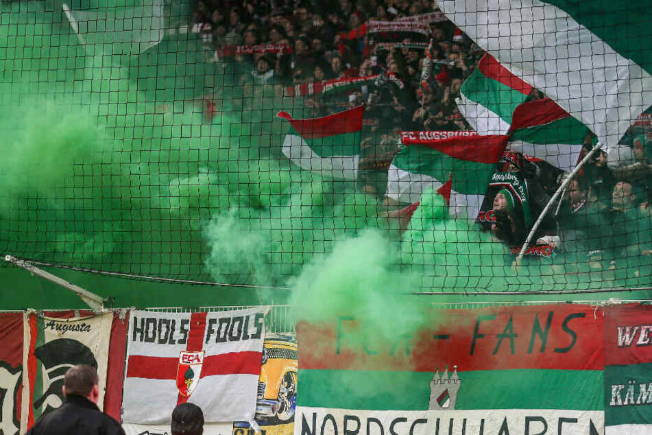 Fans aus Augsburg zünden bengalisches Feuer mit grünen Rauchwolken.