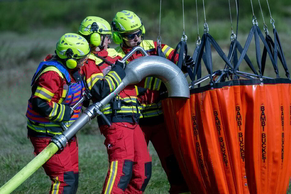 Kampf den Flammen - mit Hubschraubern: Flughelfer befüllen einen Löschsack mit neuem Wasser.