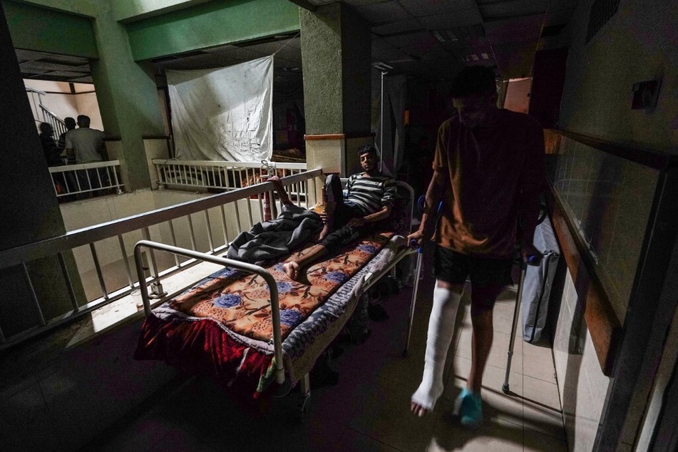 A patient lies in a bed as another walks by in a corridor lit by sunlight seeping through windows, after a partial power cut at the Al-Aqsa Martyrs Hospital in Deir al-Balah.