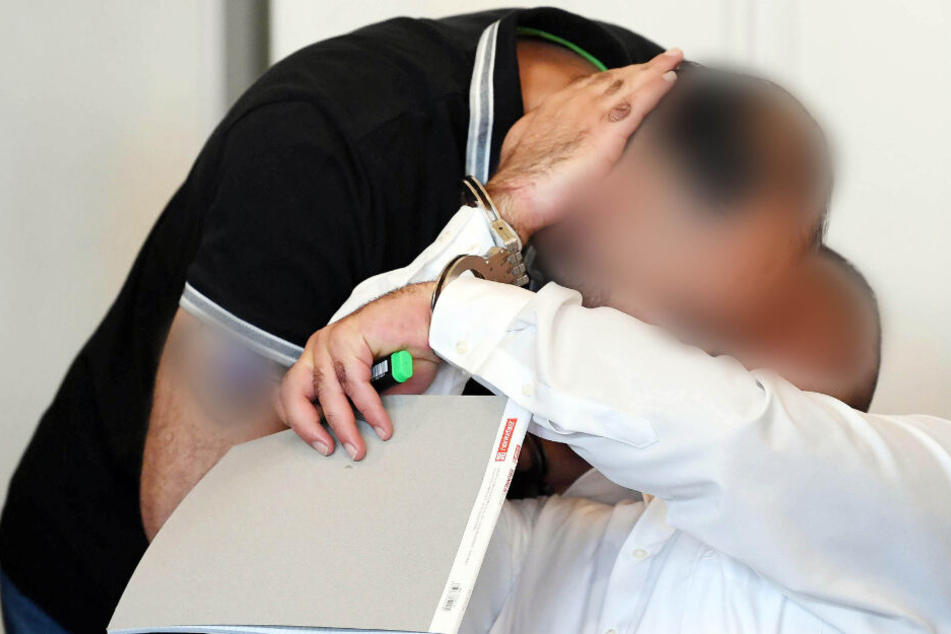 Zwei der drei Angeklagten begrüßen sich zu Prozessbeginn im Gerichtssaal.