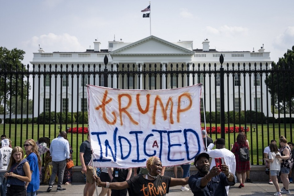 A demonstrator raises a banner reading "Trump Indicted" outside the White House in Washington DC.