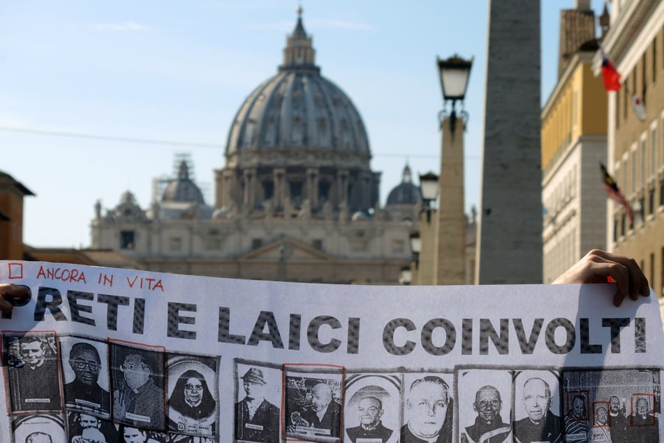 Bei einer Kundgebung halten Teilnehmer ein Schild mit Bildern von katholischen Pfarrern und Laien hoch, die für sexuellen Missbrauch verantwortlich gemacht werden.