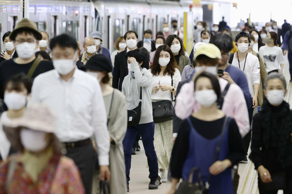 Pendler mit Gesichtsmasken laufen am Bahnhof Fukuoka im Südwesten Japans über einen Bahnsteig.