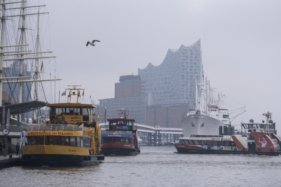 Fähren fahren bei trübem Wetter im Hafen auf der Elbe. Im Hintergrund ist die Elbphilharmonie zu sehen.