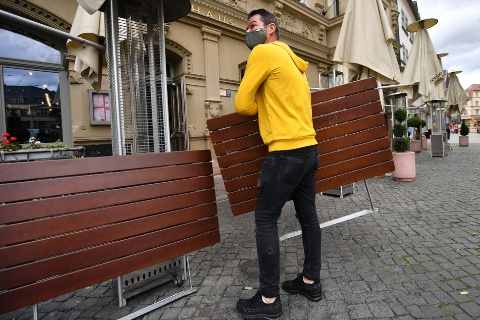 Ein Mitarbeiter eines Restaurants am Erfurter Fischmarkt stellt die Tische im Außenbereich zusammen. Wegen der Corona-Pandemie haben Restaurants, Cafés und Co. seit Wochen geschlossen.