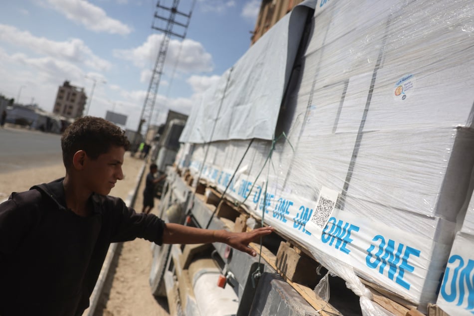 A Palestinian boy reaches out to touch a truck carrying aid provided by the World Food Programme on a road in Deir el-Balah after entering through the Kerem Shalom crossing in the southern Gaza Strip on October 17, 2025.