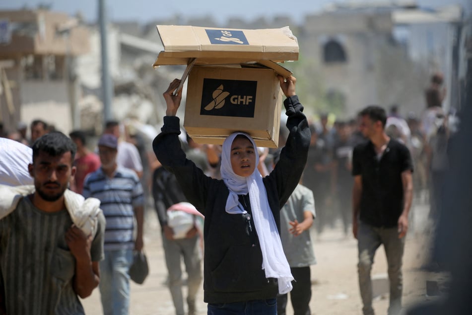 A Palestinian woman carries a food package as people return to the Nuseirat refugee camp from a US-backed Gaza Humanitarian Foundation distribution point near the Netsarim corridor in the central Gaza Strip on July 27, 2025.