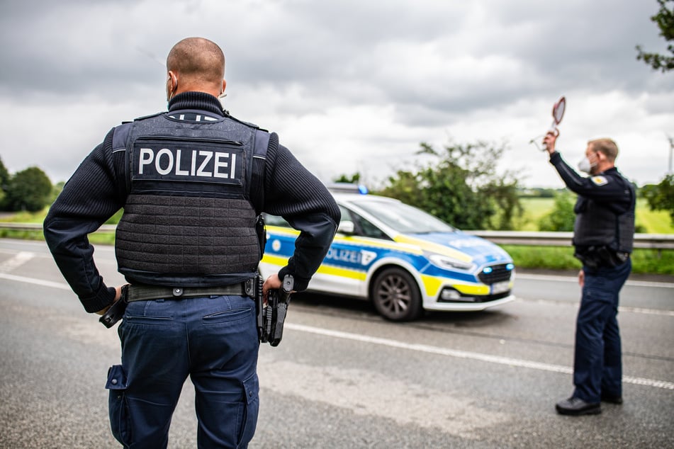 Ein Polizeibeamter steht bei einer Corona-Einreisekontrolle der Bundespolizei an der deutsch-niederländischen Grenze mit einem Polizeianhaltestab und kontrolliert Fahrzeuge im Grenzgebiet.