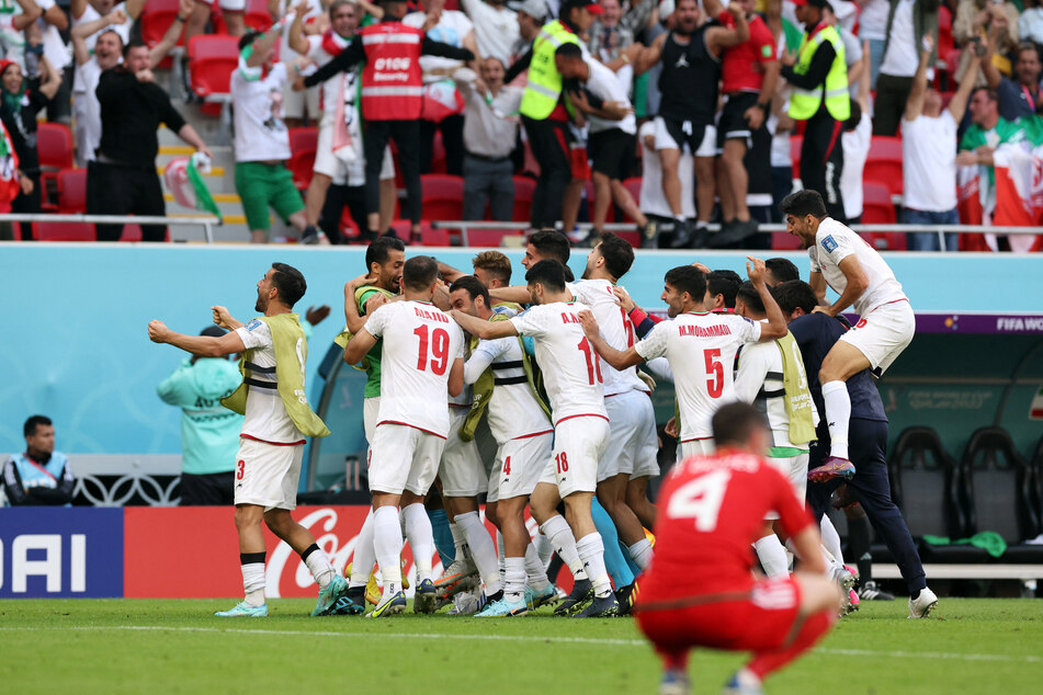 Welsh defender Ben Davies in shock as Iran's players celebrate their famous victory.