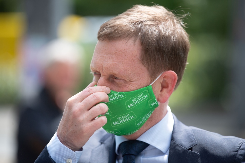 Michael Kretschmer (CDU), Ministerpräsident von Sachsen, der einen grünen Mundschutz trägt, fasst sich während der Übergabe von Schutzmasken an die Nase.