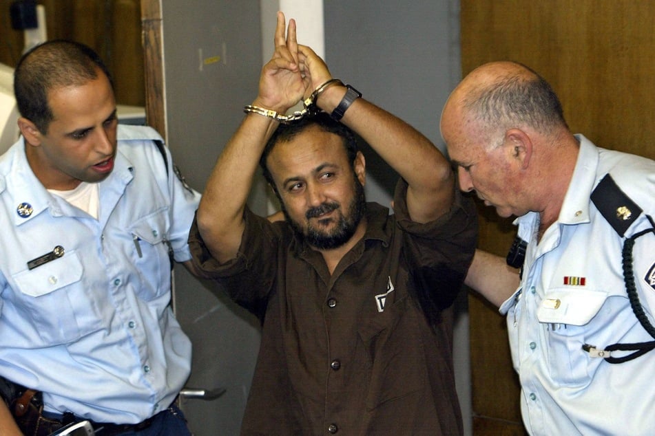 Marwan Barghouti (c.) is surrounded by Israeli officers ahead of his court proceedings in Tel Aviv on May 20, 2004.
