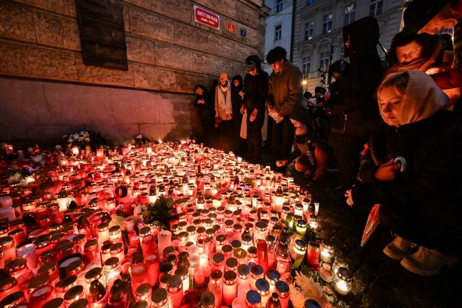 People place candles and flowers at a makeshift memorial for the the victims of the Charles University's shooting, outside the Charles University in central Prague, on December 23, 2023.