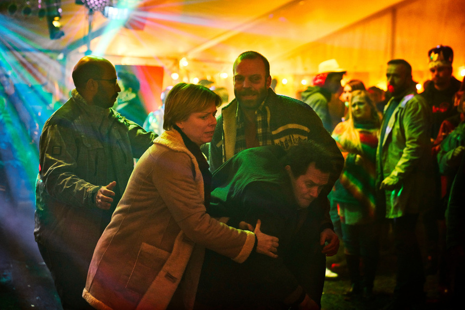 "Killing Mike" - die Dorf-Bewohner sind in Rage! Bibi (Lene Maria Christensen), John (Mads Rømer) und Milad (Dar Salim) stützen Peter (Claus Riis Østergaard), den betrunkenen Dorfarzt. Sie stehen in einem Festzelt.