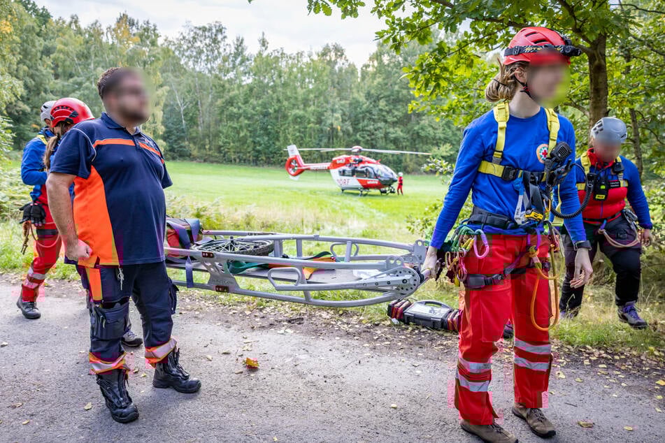 Einsatzkräfte kommen mit einer Trage zu Hilfe. Im Hintergrund steht schon der Rettungshelikopter bereit.