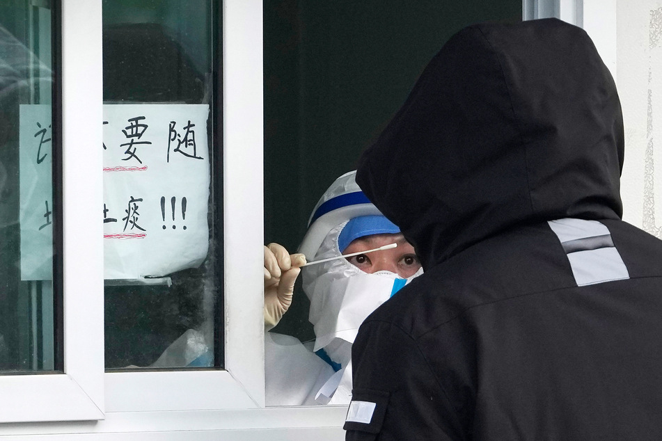 Eine Mitarbeiterin mit Gesichtsschutz entnimmt in Peking einer Person einen Corona-Abstrich.