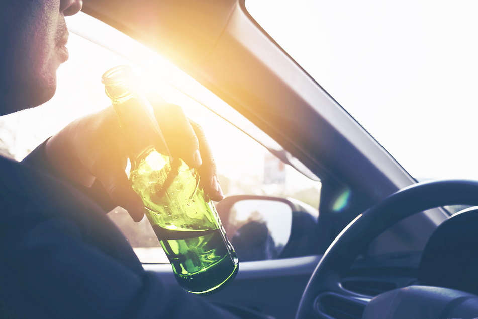 Ein Mann trinkt Bier, während er mit dem Auto fährt (Symbolbild).