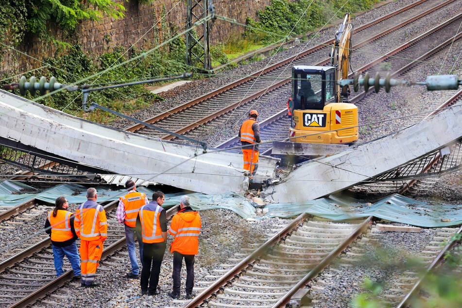 Arbeiter untersuchen Teile einer Brücke, die auf den Gleisen liegen.