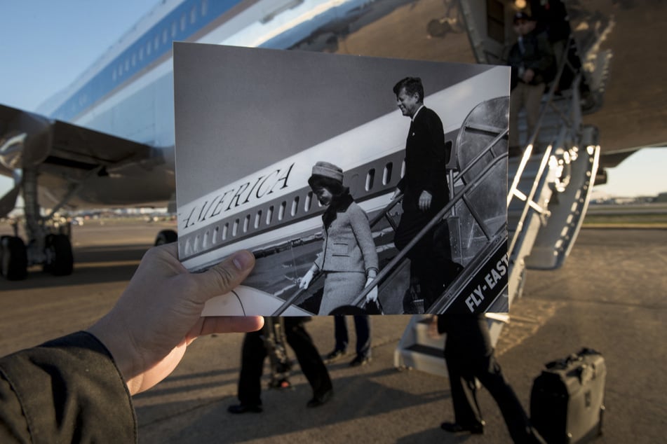 A historic photo dated November 22, 1963 showing former President John F. Kennedy and First Lady Jacqueline Kennedy arriving in Dallas, Texas (Cecil Stoughton, White House Photographs, John F. Kennedy Presidential Library and Museum, Boston) is held up by the photographer against Air Force One.