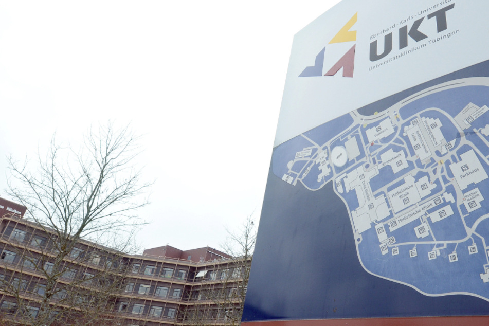 Ein Logo mit einem Hinweisschild des Universitätsklinikums Tübingen steht vor einem Klinikgebäude.