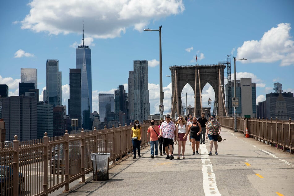People walk maskless on the Brooklyn Bridge after the governor announced the immediate lifting of major COVID-19 restrictions across the state.