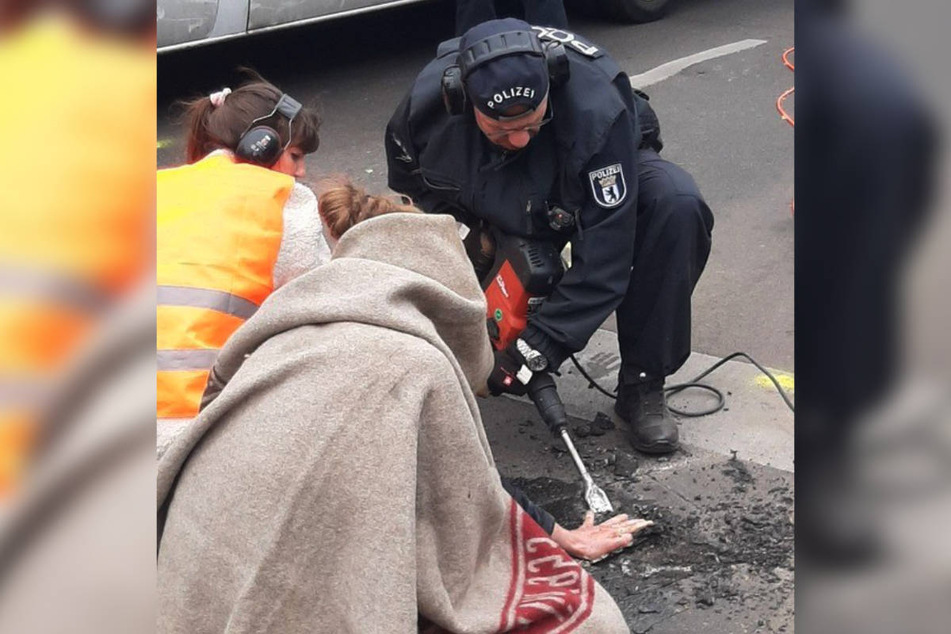 Ein Polizist muss den Straßenbelag auf dem Mühlendamm mit einem Presslufthammer aufstemmen, um einen Klimaaktivisten zu entfernen.