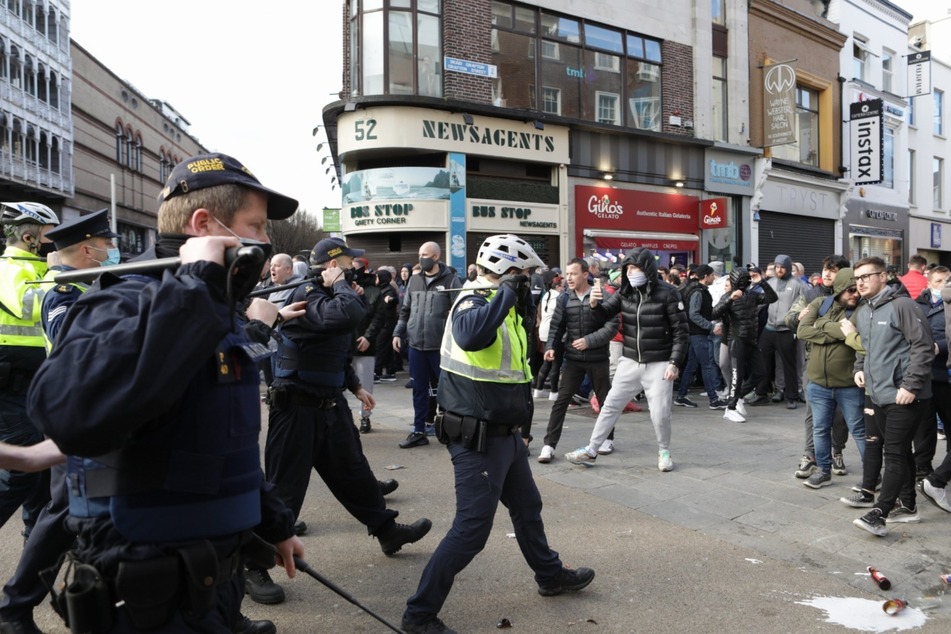 Polizeibeamte der Garda Siochana gehen während eines Protests gegen den coronabedingten Lockdown mit Schlagstöcken in der Hand auf Demonstranten zu.