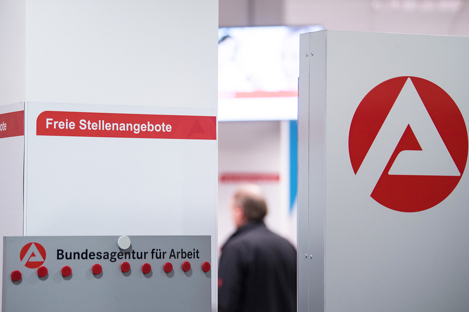 Ein Mann steht am im Wartebereich hinter einer Stellwand für Stellenangebote.