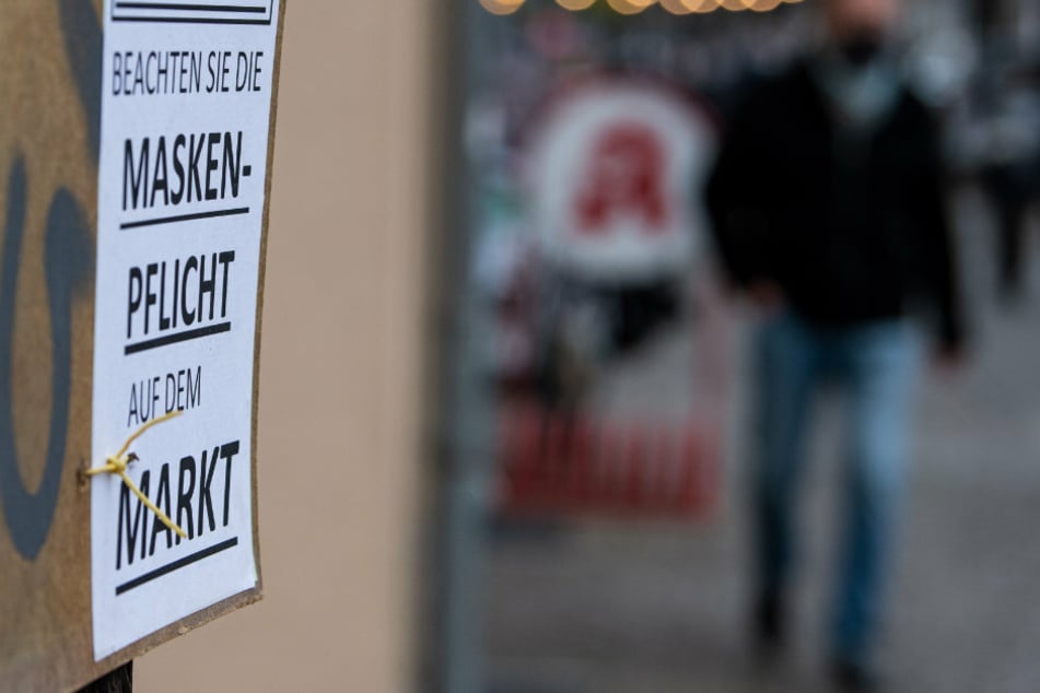 An einem Baum hängt ein Schild mit der Aufschrift „Achtung - Beachten Sie die Maskenpflicht auf dem Markt“.