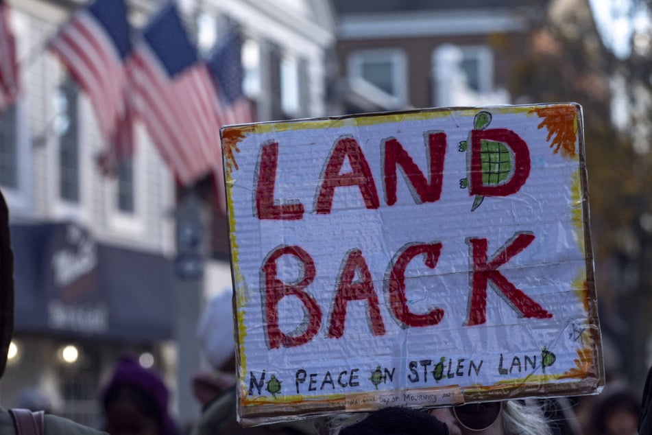 A participant raises a sign calling for "Land Back" during the 2025 National Day of Mourning.