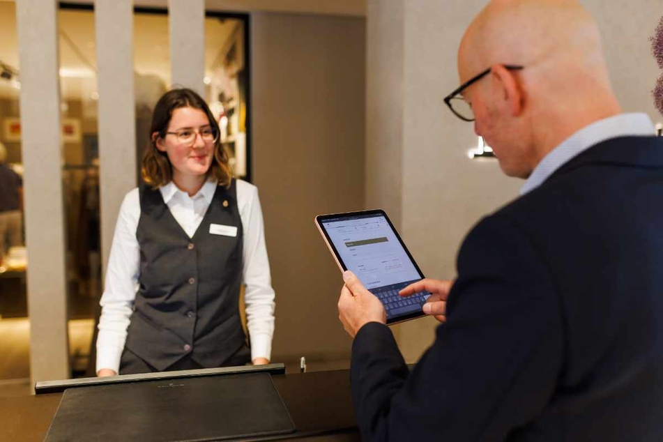 Donaueschingen: Eine Rezeptionistin steht an der Rezeption des Hotel "Öschberghof", während ein Gast im Vordergrund einen digitalen Meldeschein des Hotels ausfüllt.